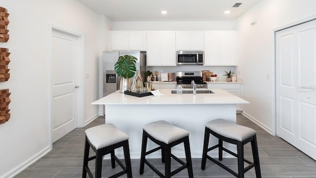 kitchen with white cabinets, appliances with stainless steel finishes, a kitchen breakfast bar, and an island with sink