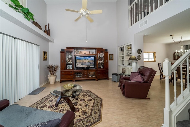 living room featuring light hardwood / wood-style flooring, a towering ceiling, and ceiling fan with notable chandelier