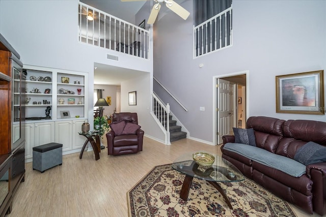 living room with ceiling fan, a towering ceiling, and light hardwood / wood-style flooring