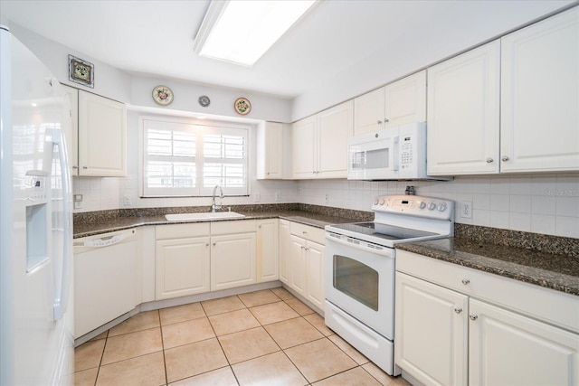 kitchen with white appliances, dark stone counters, sink, light tile patterned floors, and white cabinetry