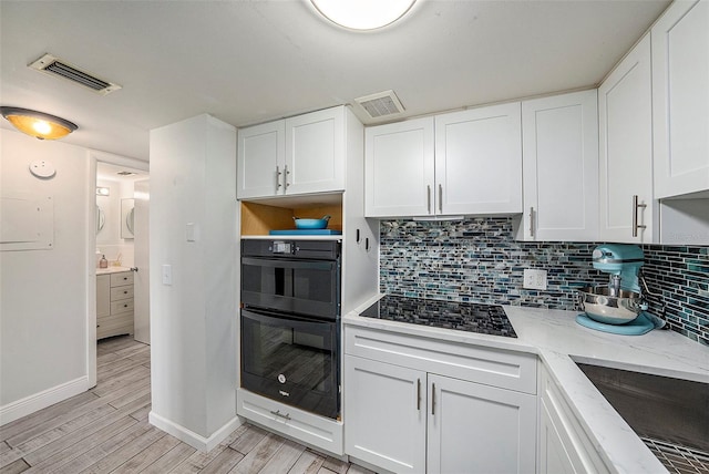 kitchen featuring decorative backsplash, white cabinetry, black appliances, and light stone counters