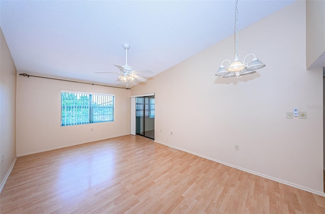 empty room with ceiling fan with notable chandelier, light hardwood / wood-style floors, and lofted ceiling