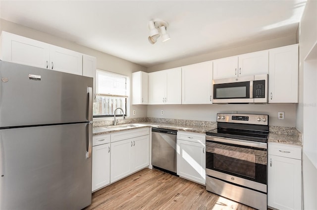 kitchen with sink, stainless steel appliances, light stone counters, white cabinets, and light wood-type flooring