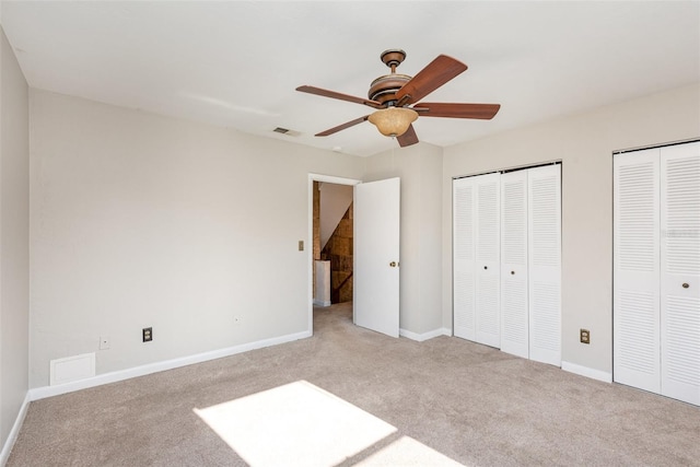 unfurnished bedroom featuring ceiling fan, light colored carpet, and two closets