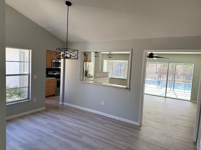 unfurnished dining area featuring ceiling fan with notable chandelier, light hardwood / wood-style flooring, a wealth of natural light, and lofted ceiling