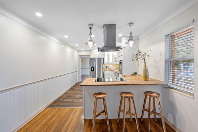 kitchen with hanging light fixtures, kitchen peninsula, stainless steel fridge, a breakfast bar area, and island range hood