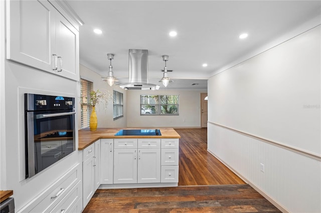 kitchen with butcher block counters, hanging light fixtures, island exhaust hood, oven, and white cabinets