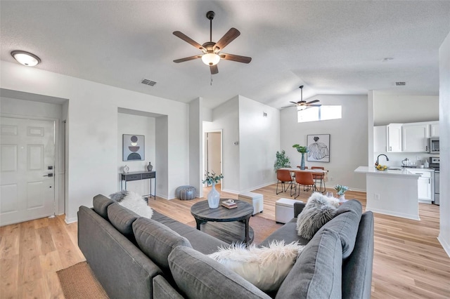 living room with ceiling fan, sink, light hardwood / wood-style flooring, a textured ceiling, and lofted ceiling