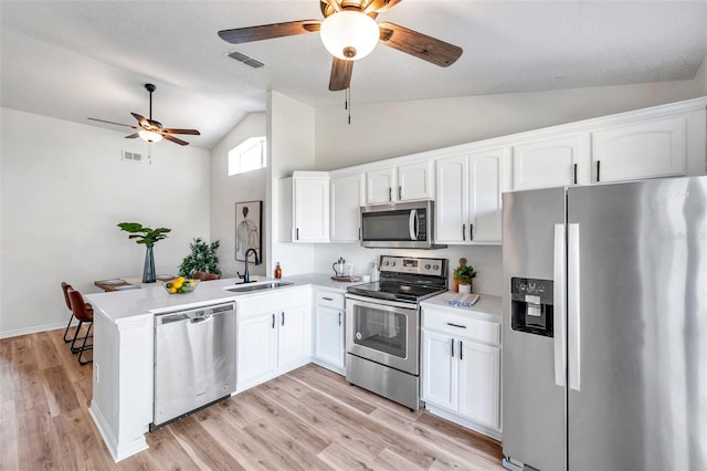 kitchen with white cabinets, sink, vaulted ceiling, appliances with stainless steel finishes, and kitchen peninsula