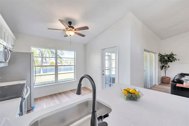 kitchen with vaulted ceiling, ceiling fan, sink, range, and white cabinetry