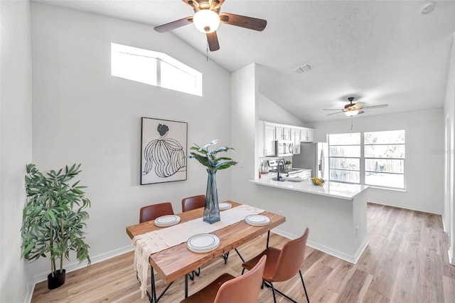 dining space featuring a textured ceiling, vaulted ceiling, sink, and light hardwood / wood-style flooring