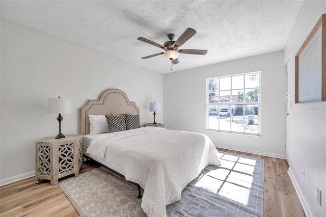 bedroom featuring ceiling fan, light hardwood / wood-style floors, and a textured ceiling