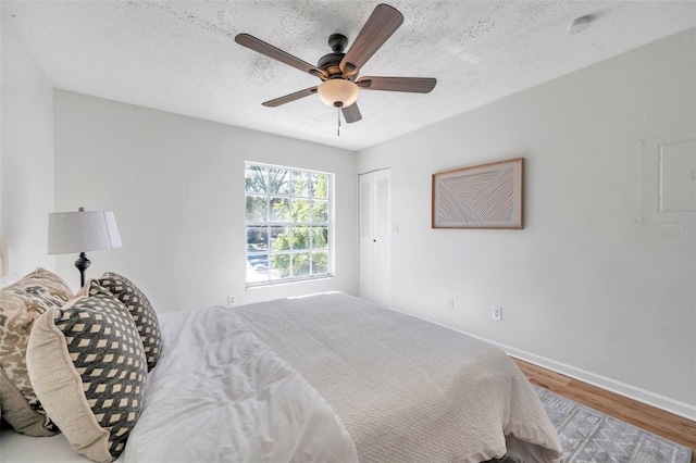 bedroom with electric panel, light hardwood / wood-style flooring, ceiling fan, a textured ceiling, and a closet