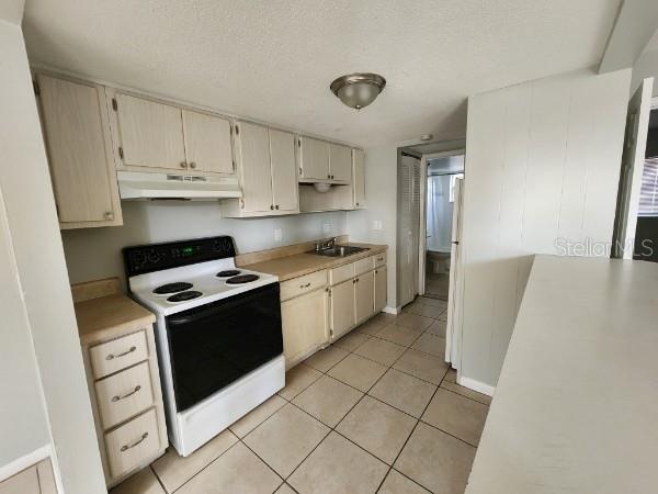 kitchen featuring a textured ceiling, sink, cream cabinets, white range with electric cooktop, and light tile patterned flooring