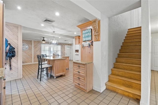 kitchen featuring a textured ceiling, a center island with sink, hanging light fixtures, a breakfast bar area, and wood walls