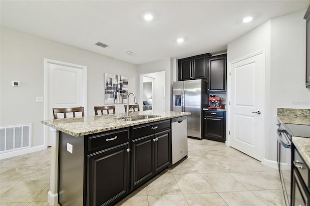 kitchen with light stone countertops, a kitchen breakfast bar, stainless steel appliances, a kitchen island with sink, and sink