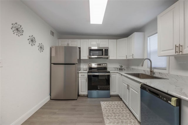 kitchen featuring light stone countertops, white cabinetry, stainless steel appliances, light hardwood / wood-style floors, and sink