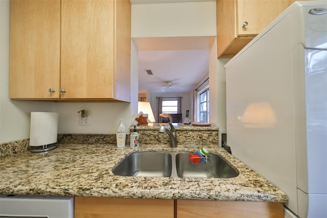 kitchen featuring sink, light brown cabinetry, white fridge, light stone counters, and kitchen peninsula