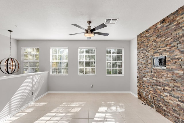 tiled empty room featuring a textured ceiling, a wood stove, a wall unit AC, and ceiling fan with notable chandelier