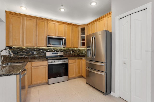 kitchen featuring backsplash, sink, dark stone countertops, light tile patterned floors, and stainless steel appliances