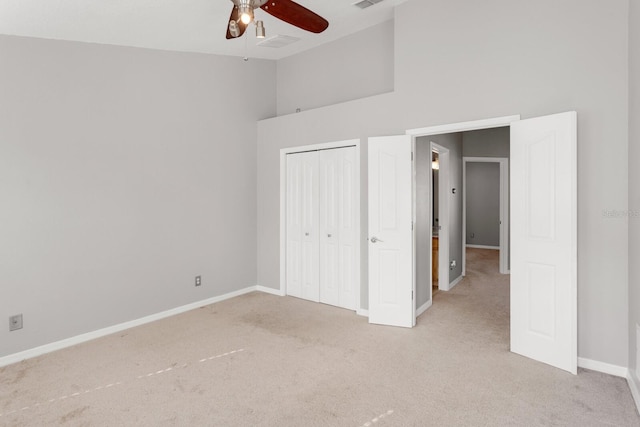 unfurnished bedroom with ceiling fan, a closet, a towering ceiling, and light colored carpet