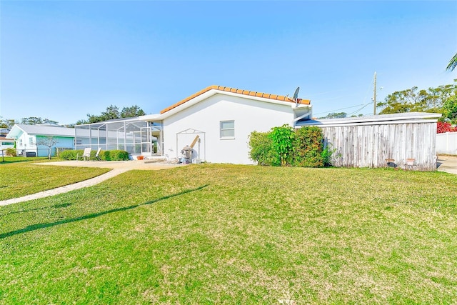 rear view of house featuring a lawn and glass enclosure