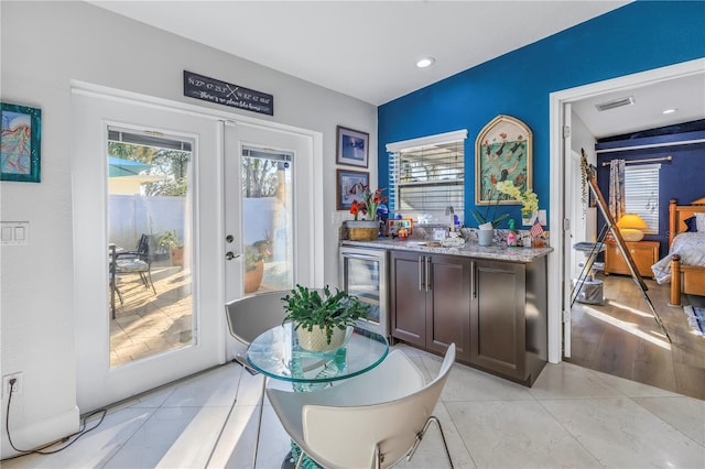 bar with french doors, dark brown cabinets, beverage cooler, a healthy amount of sunlight, and light tile patterned floors