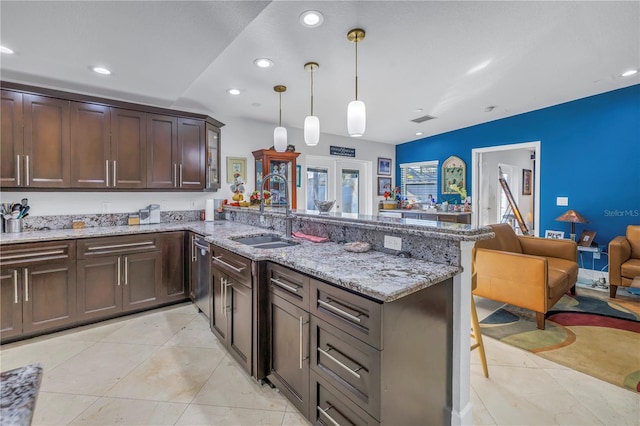 kitchen featuring dark brown cabinetry, sink, light stone counters, kitchen peninsula, and decorative light fixtures