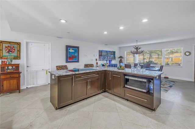 kitchen featuring a kitchen island with sink, light stone counters, hanging light fixtures, and a chandelier