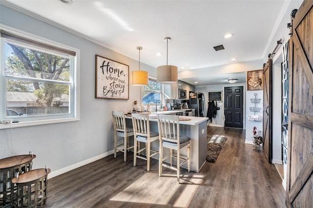 kitchen with a kitchen bar, decorative light fixtures, dark hardwood / wood-style floors, kitchen peninsula, and a barn door