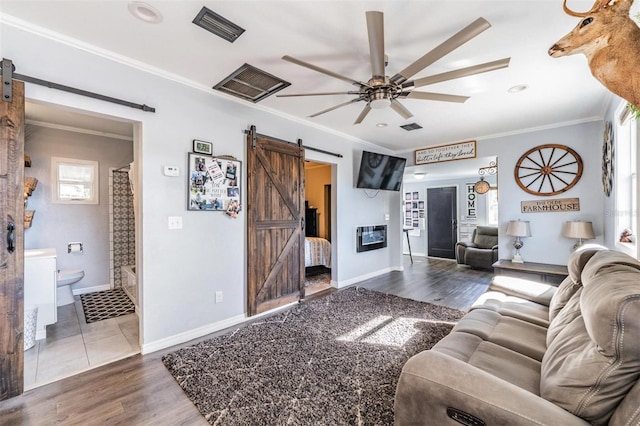 living room featuring dark hardwood / wood-style floors, ceiling fan, ornamental molding, and a barn door