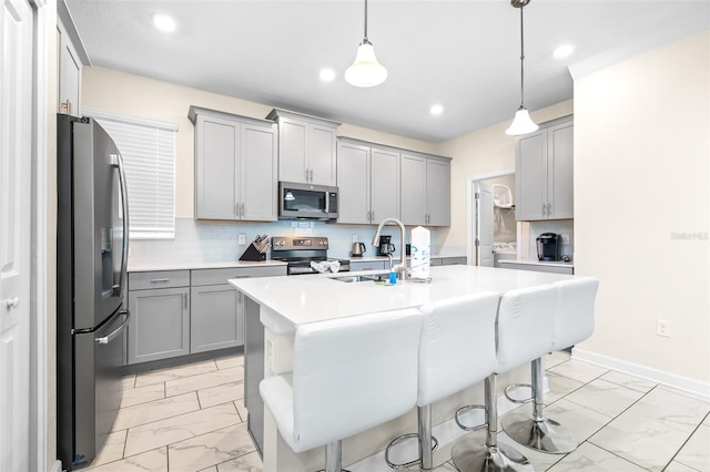 kitchen with gray cabinetry, pendant lighting, a kitchen island with sink, a kitchen bar, and stainless steel appliances