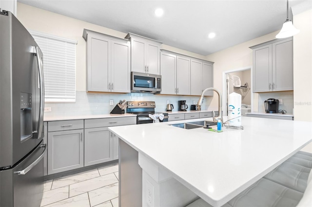 kitchen with gray cabinetry, a center island with sink, a kitchen breakfast bar, sink, and appliances with stainless steel finishes