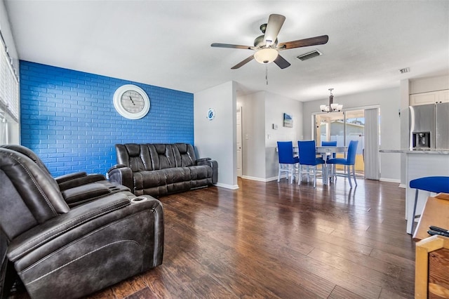 living room featuring ceiling fan with notable chandelier, dark wood-type flooring, and brick wall