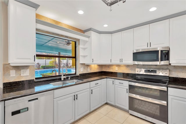 kitchen with stainless steel appliances, light tile patterned floors, decorative backsplash, white cabinetry, and sink