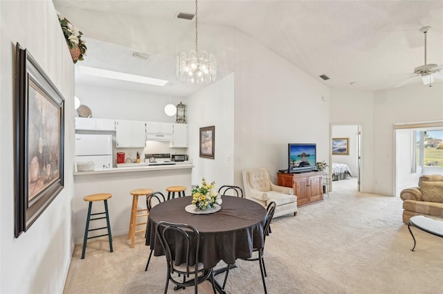 carpeted dining space with lofted ceiling with skylight and ceiling fan with notable chandelier