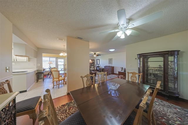 dining area with ceiling fan with notable chandelier, a textured ceiling, and light wood-type flooring