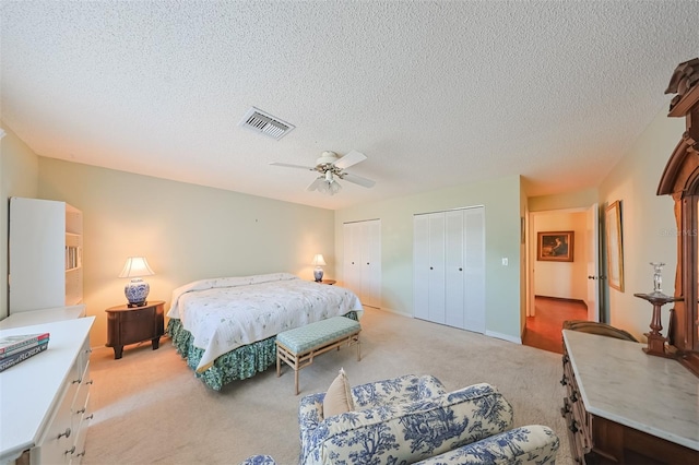 carpeted bedroom featuring multiple closets, ceiling fan, and a textured ceiling