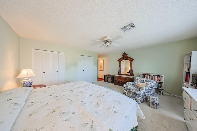 carpeted bedroom featuring a textured ceiling, ceiling fan, and two closets