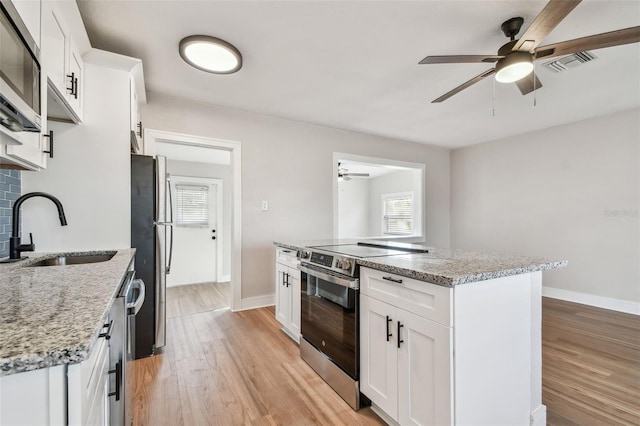 kitchen featuring white cabinetry, sink, stainless steel appliances, light stone counters, and an island with sink