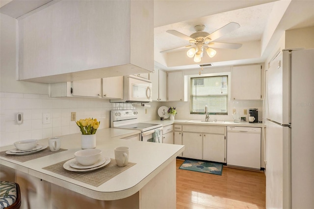 kitchen with white appliances, sink, light hardwood / wood-style flooring, tasteful backsplash, and kitchen peninsula