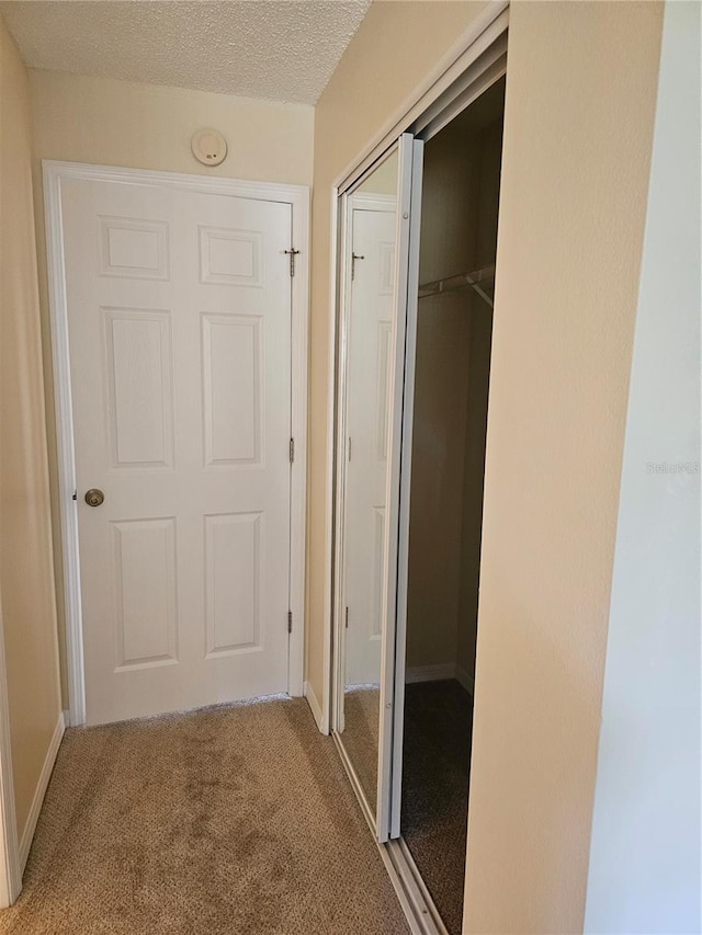 corridor with light carpet and a textured ceiling