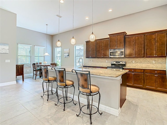 kitchen featuring stainless steel appliances, a center island with sink, decorative light fixtures, and sink