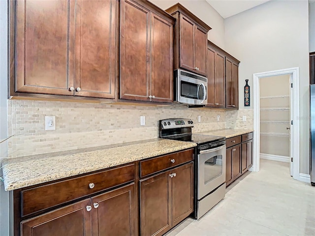 kitchen featuring appliances with stainless steel finishes, light stone countertops, tasteful backsplash, and dark brown cabinetry