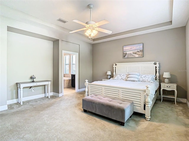 bedroom featuring ceiling fan, ensuite bath, and a tray ceiling