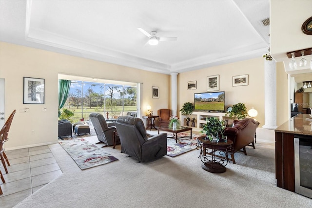 tiled living room with ceiling fan, ornate columns, beverage cooler, and a tray ceiling