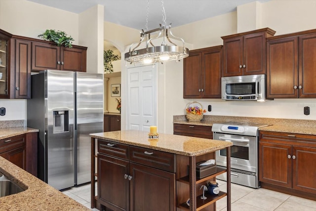 kitchen featuring appliances with stainless steel finishes, light stone counters, dark brown cabinetry, light tile patterned floors, and decorative light fixtures