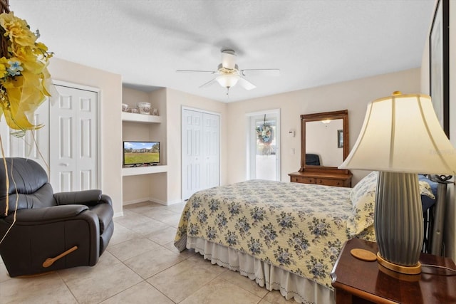 bedroom featuring ceiling fan, light tile patterned flooring, a textured ceiling, and multiple closets