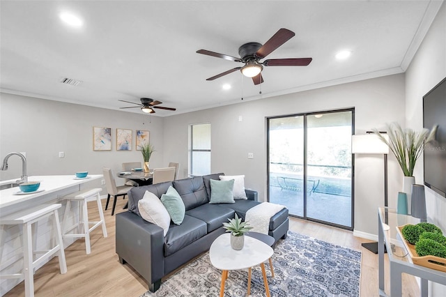 living room with light wood-type flooring, ceiling fan, crown molding, and sink