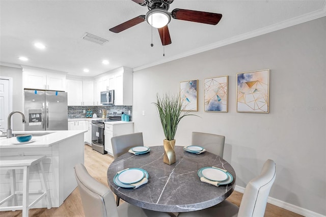 dining room with sink, ceiling fan, crown molding, and light hardwood / wood-style flooring